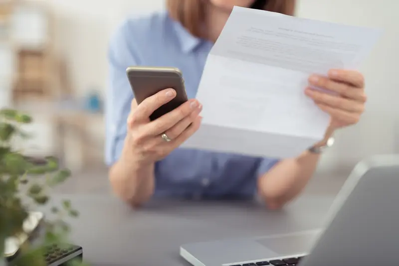 Person hält ein Schreiben und ihr Smartphone in den Händen