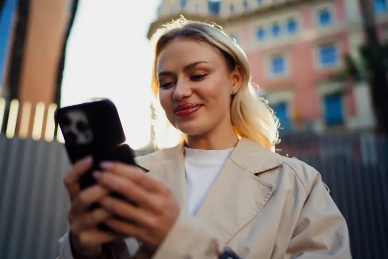 Junge Frau schaut in der Stadt lächelnd auf ihr Smartphone