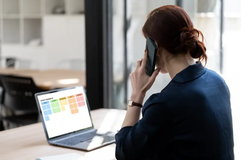 Frau telefoniert am Schreibtisch, auf ihrem Laptop ist ein Kalender geöffnet