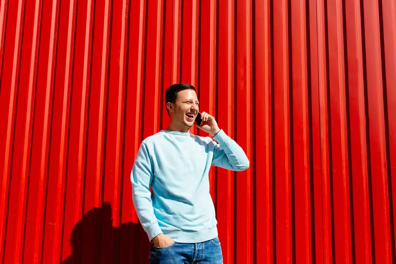 Lachender Mann telefoniert vor einer roten Wand