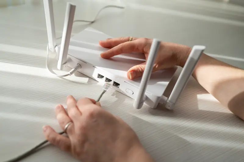 Hände stecken ein Netzwerkkabel in einen weißen WLAN-Router mit Antennen